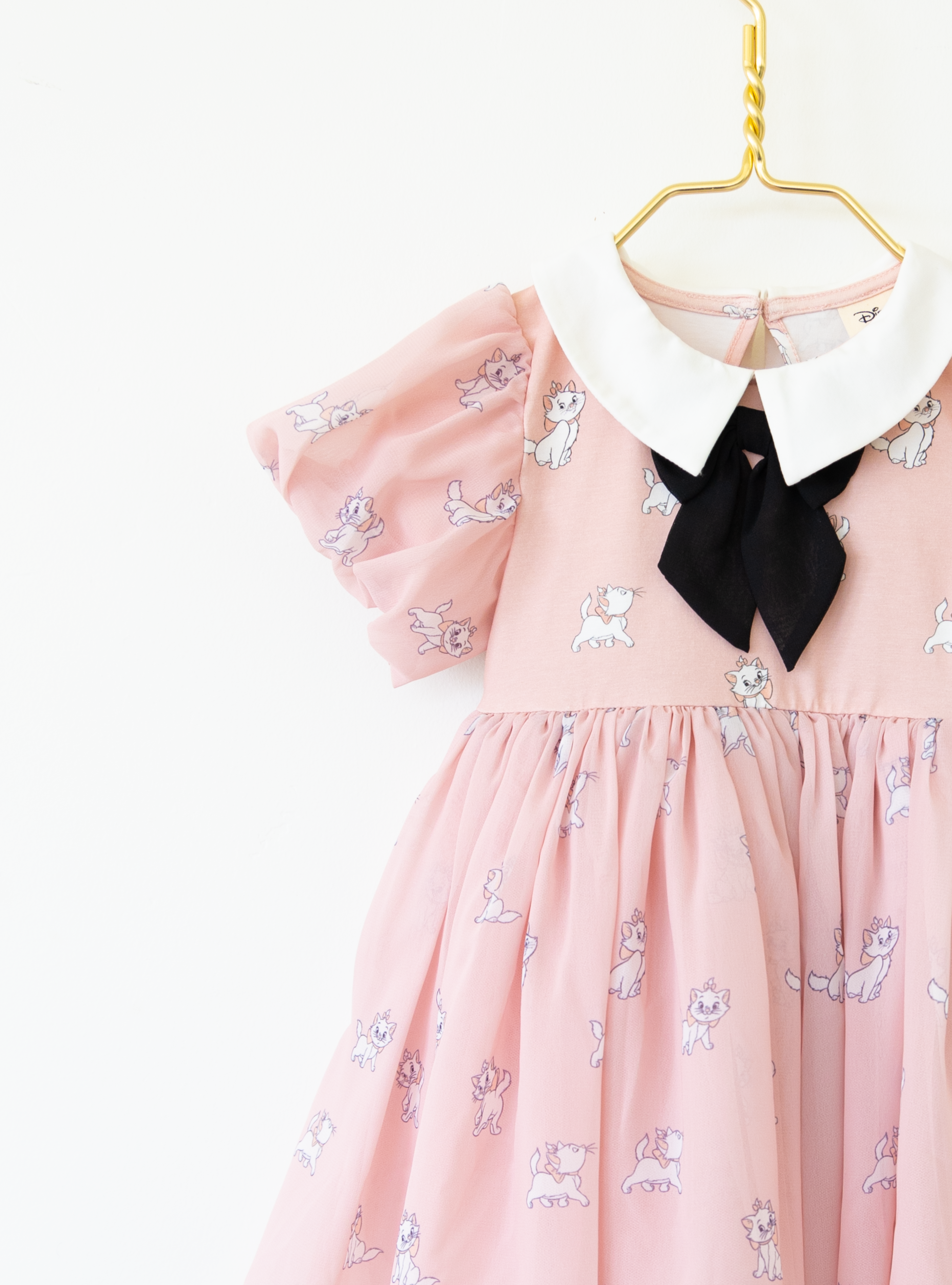 Disney and Taylor Joelle branded Marie Dress with Marie printed all around. This dress has puff chiffon sleeves, and a high waited puff chiffon skirt. Along with that, it has a collar with a black bow, and trim on the bottom of the dress.