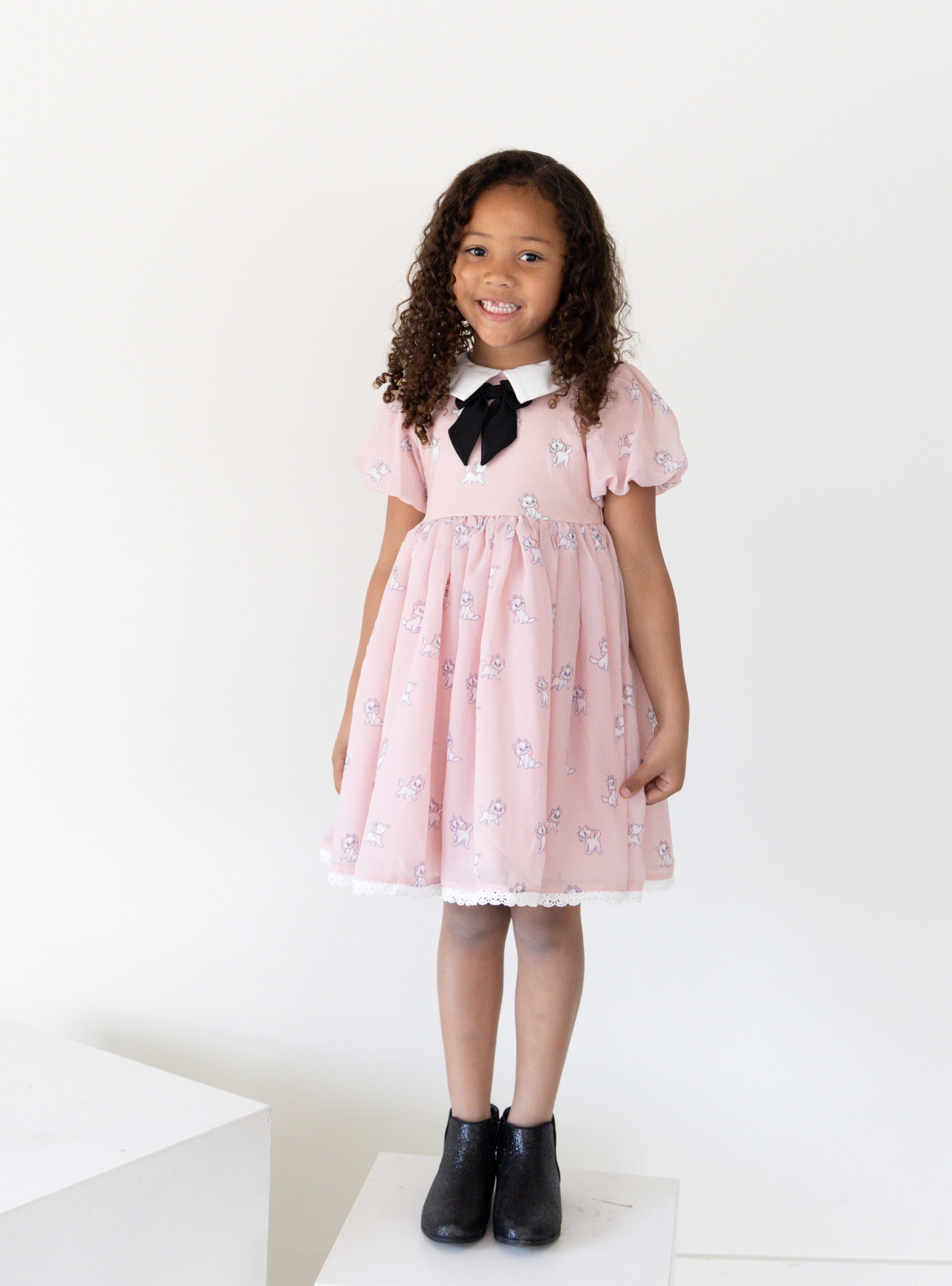 Disney and Taylor Joelle branded Marie Dress with Marie printed all around. This dress has puff chiffon sleeves, and a high waited puff chiffon skirt. Along with that, it has a collar with a black bow, and trim on the bottom of the dress.