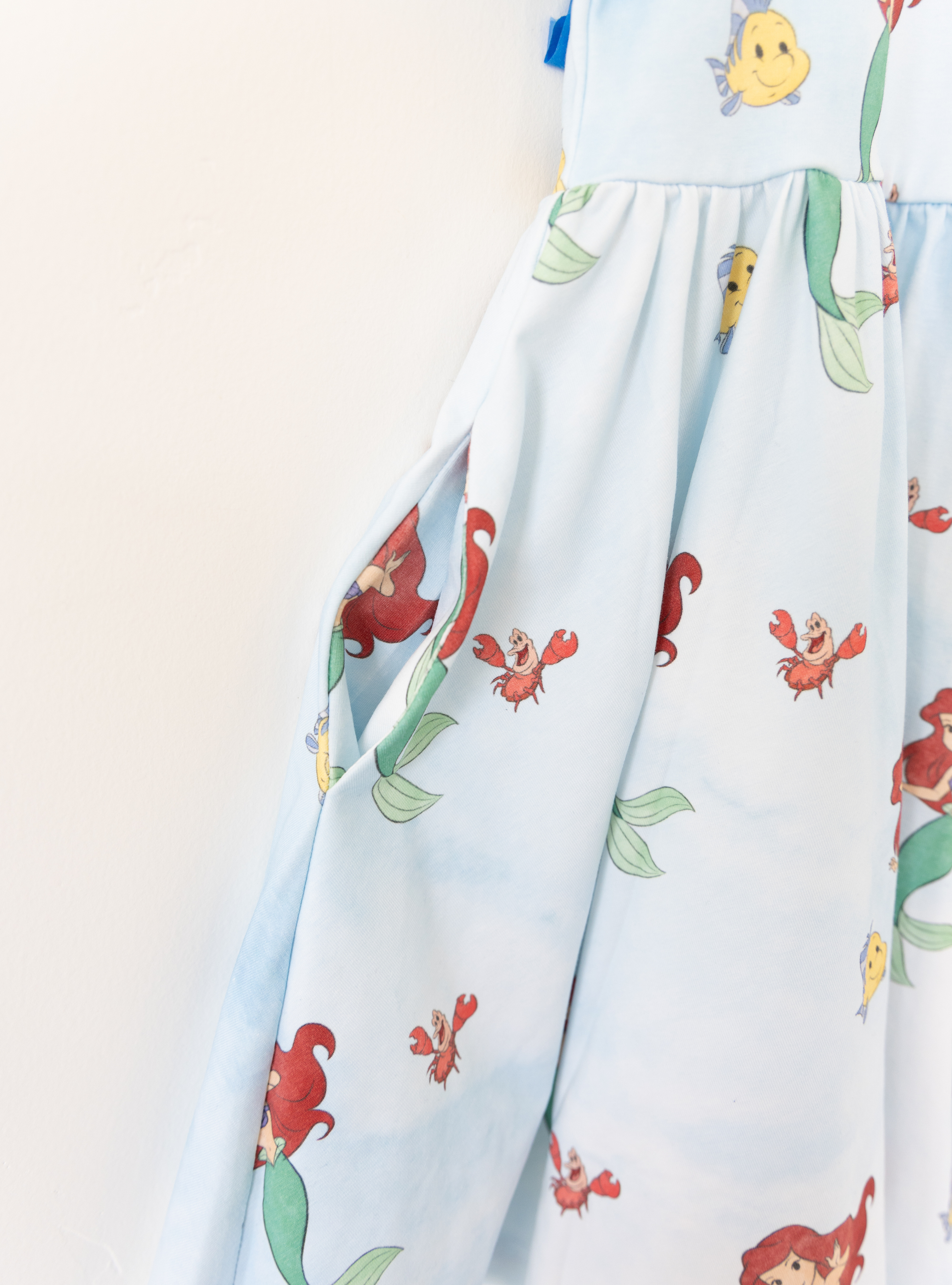 Disney and Taylor Joelle branded Ariel dress with an Ariel, Flounder, and Sebastian print all around. This dress has pockets.